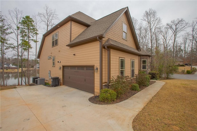 view of side of home featuring central AC unit, a shingled roof, concrete driveway, a garage, and a water view