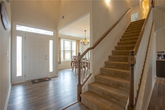 entrance foyer featuring visible vents, stairway, a towering ceiling, an inviting chandelier, and dark wood-style flooring