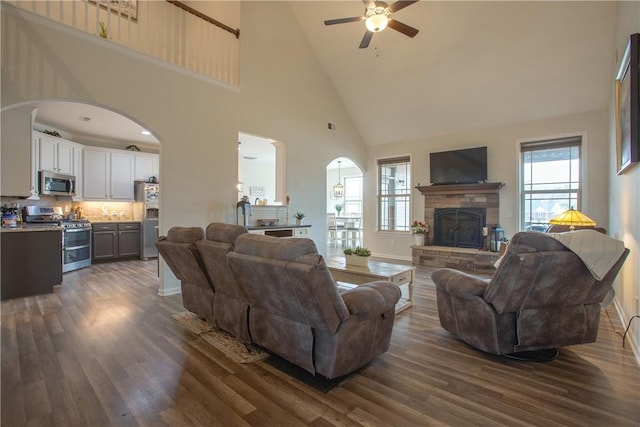 living room with a wealth of natural light, arched walkways, dark wood-type flooring, and a ceiling fan