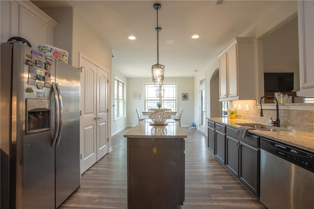 kitchen with light stone counters, a kitchen island, a sink, stainless steel appliances, and tasteful backsplash