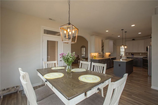 dining room with arched walkways, a notable chandelier, recessed lighting, and dark wood-type flooring