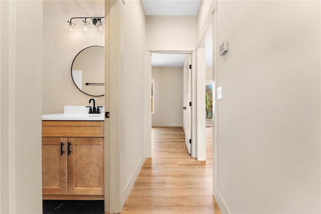 hallway with light wood-style flooring, baseboards, and a sink