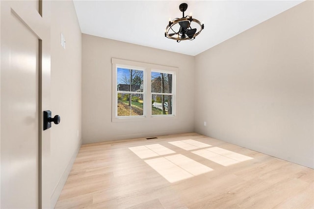 empty room featuring a notable chandelier, visible vents, and wood finished floors