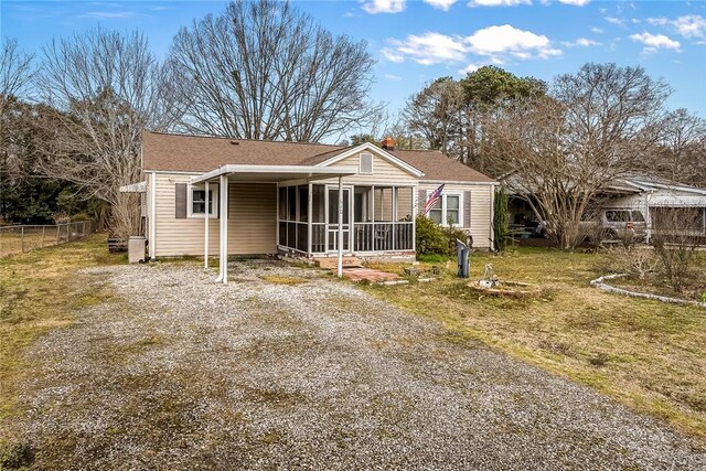 rear view of house with driveway, fence, a yard, a sunroom, and a carport