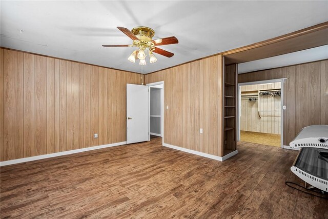 unfurnished bedroom featuring wood walls, a ceiling fan, baseboards, and wood finished floors