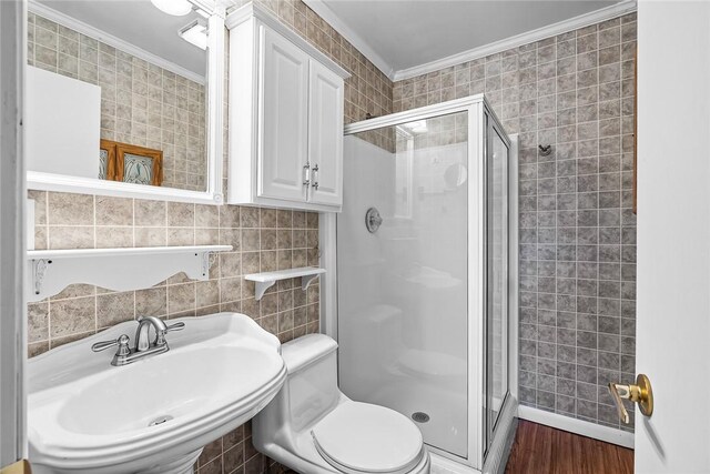 full bath featuring wood finished floors, a stall shower, a sink, crown molding, and tile walls
