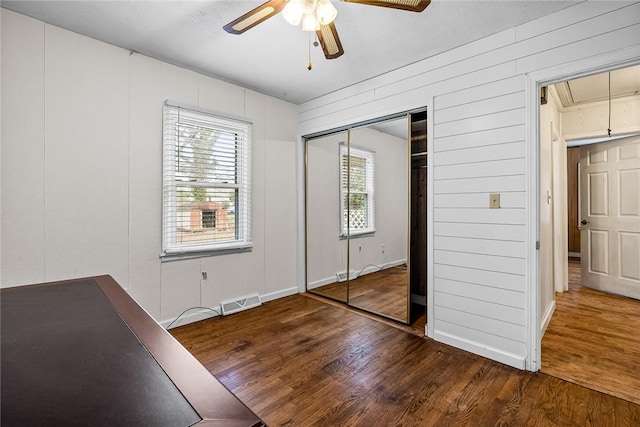 unfurnished bedroom featuring attic access, multiple windows, wood finished floors, and visible vents
