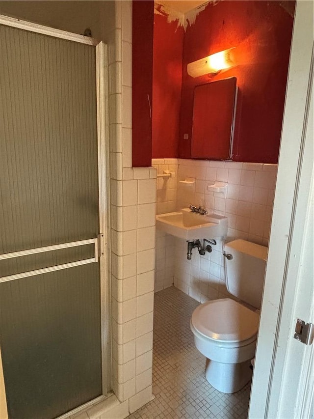 bathroom with a shower stall, a wainscoted wall, toilet, tile patterned floors, and tile walls