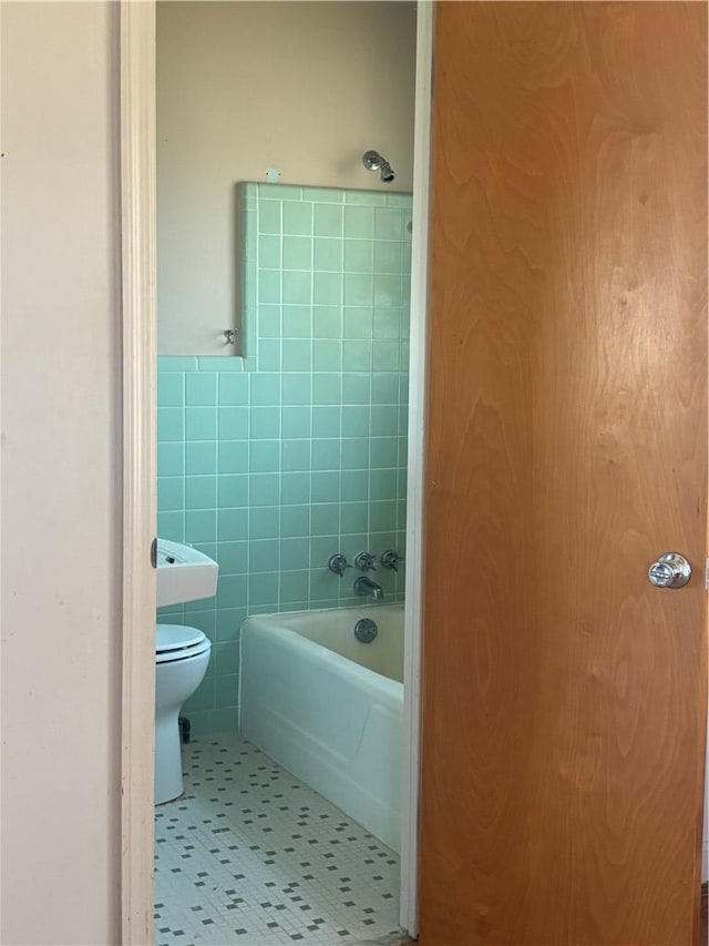 bathroom featuring a wainscoted wall, toilet, shower / bath combination, tile patterned floors, and tile walls