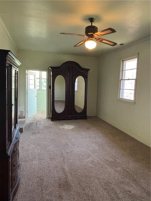 unfurnished bedroom featuring multiple windows, carpet floors, ceiling fan, and crown molding