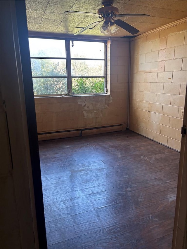empty room featuring a baseboard radiator, concrete block wall, ceiling fan, and dark wood finished floors