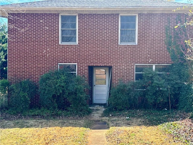 view of front of property featuring brick siding and roof with shingles