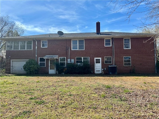 back of house with cooling unit, an attached garage, a chimney, a lawn, and brick siding