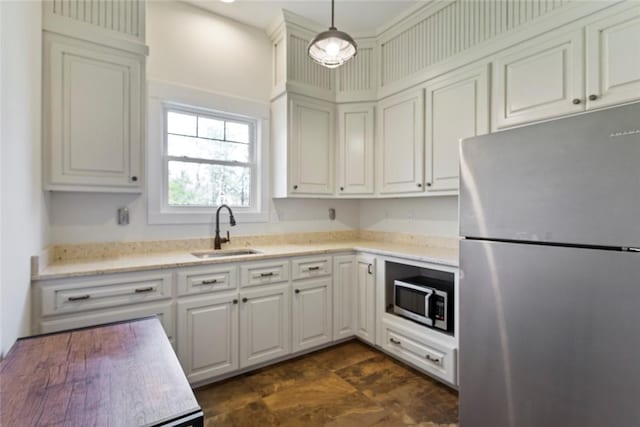 kitchen featuring light stone countertops, a sink, stainless steel appliances, white cabinetry, and hanging light fixtures