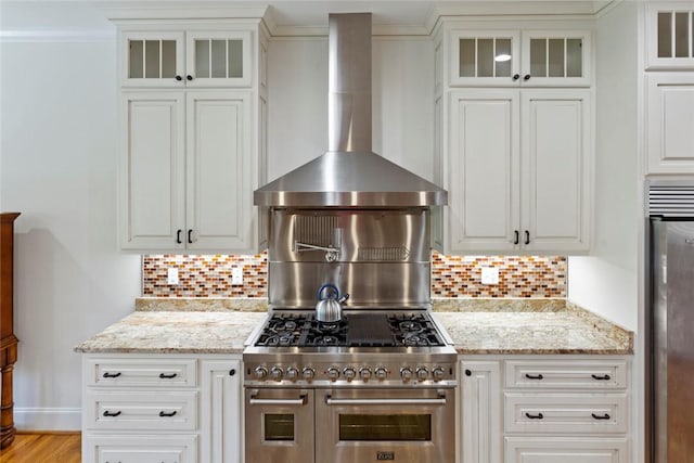kitchen with stainless steel appliances, decorative backsplash, white cabinetry, light stone counters, and wall chimney range hood