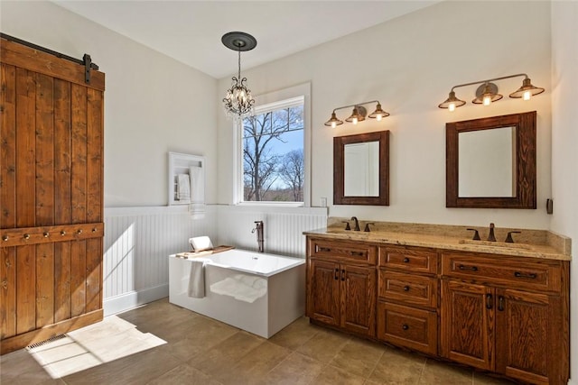 full bath with double vanity, a sink, a freestanding tub, and wainscoting