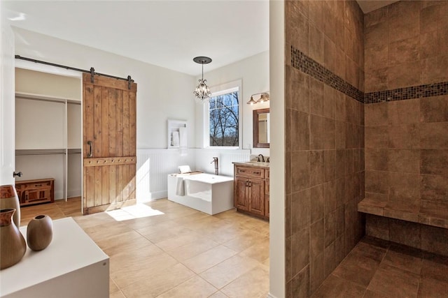 full bath with a chandelier, a garden tub, vanity, tile patterned flooring, and wainscoting