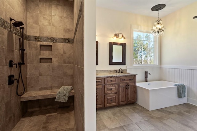 full bath featuring tiled shower, a freestanding tub, a wainscoted wall, vanity, and a notable chandelier