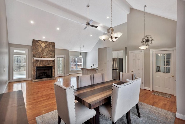dining room with a ceiling fan, beam ceiling, a fireplace, and light wood-type flooring