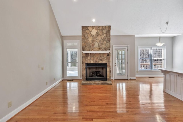 unfurnished living room featuring baseboards, light wood-style flooring, vaulted ceiling, and a stone fireplace