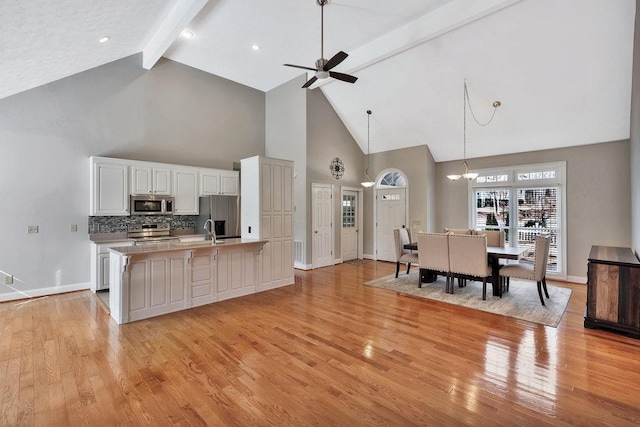 kitchen featuring white cabinets, stainless steel appliances, a ceiling fan, beam ceiling, and light wood-style floors