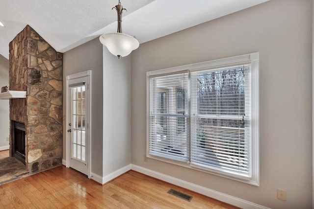 unfurnished dining area with baseboards, a textured ceiling, visible vents, a stone fireplace, and wood finished floors