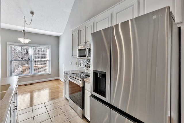 kitchen with lofted ceiling, light tile patterned floors, stainless steel appliances, a textured ceiling, and white cabinets