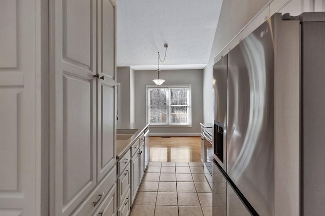 kitchen with a textured ceiling, baseboards, stainless steel appliances, pendant lighting, and light tile patterned floors