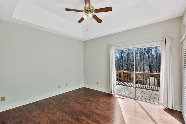 unfurnished room with a ceiling fan, a raised ceiling, baseboards, and wood finished floors