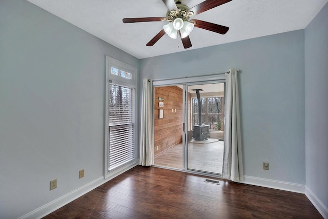 unfurnished room featuring a wood stove, baseboards, ceiling fan, visible vents, and wood finished floors