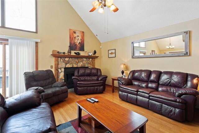living room featuring a stone fireplace, ceiling fan with notable chandelier, high vaulted ceiling, and wood finished floors