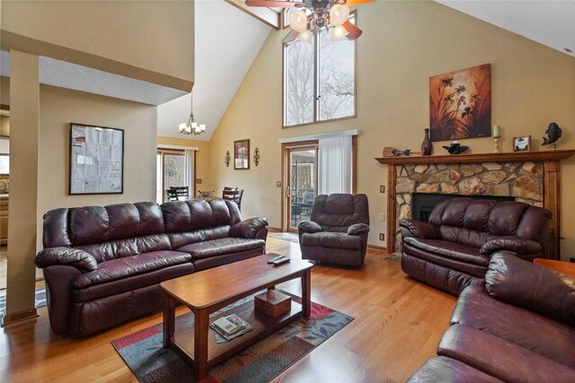 living room with high vaulted ceiling, a stone fireplace, baseboards, ceiling fan with notable chandelier, and light wood-style floors