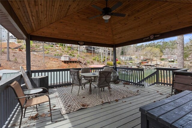 wooden terrace with a water view, a gazebo, outdoor dining space, and a ceiling fan