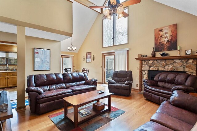living room with high vaulted ceiling, light wood-style flooring, baseboards, a fireplace, and ceiling fan with notable chandelier