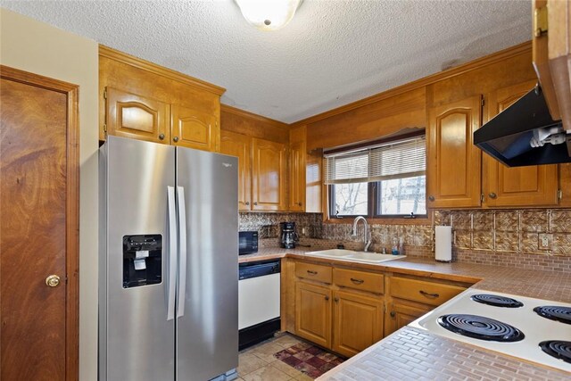 kitchen with white appliances, brown cabinets, under cabinet range hood, a sink, and backsplash