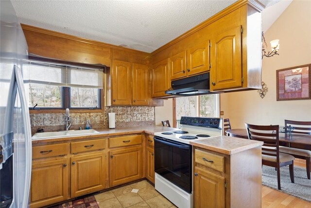 kitchen featuring light countertops, a sink, white electric stove, tasteful backsplash, and under cabinet range hood