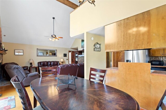 dining room with ceiling fan, high vaulted ceiling, light wood-type flooring, and a fireplace with raised hearth