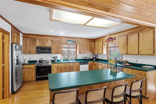 kitchen featuring a kitchen breakfast bar, appliances with stainless steel finishes, brown cabinets, light wood-type flooring, and dark countertops