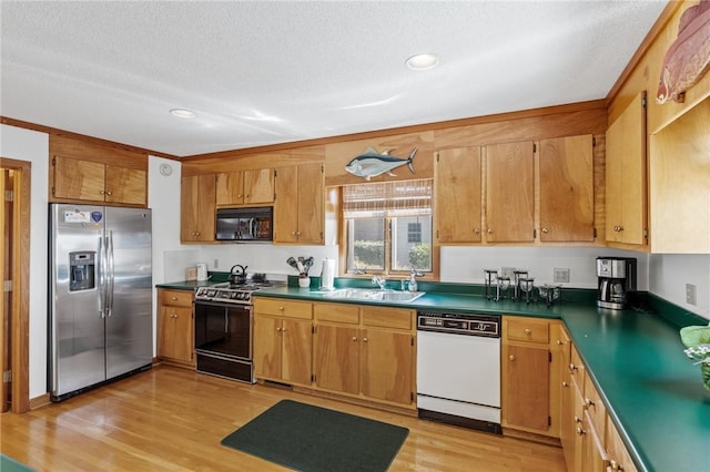 kitchen with stainless steel appliances, a textured ceiling, a sink, dark countertops, and light wood-style floors