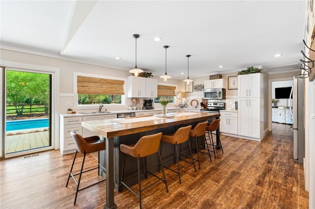 kitchen with stainless steel microwave, a wealth of natural light, wooden counters, and a breakfast bar area