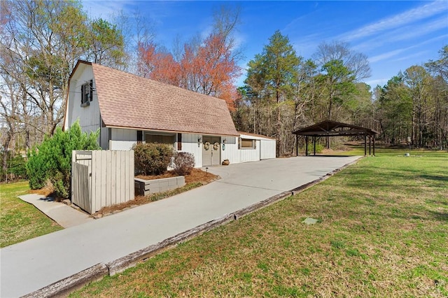 view of side of property with a gambrel roof, concrete driveway, a shingled roof, a yard, and a detached carport