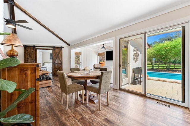 dining room with a barn door, vaulted ceiling, visible vents, a ceiling fan, and wood finished floors
