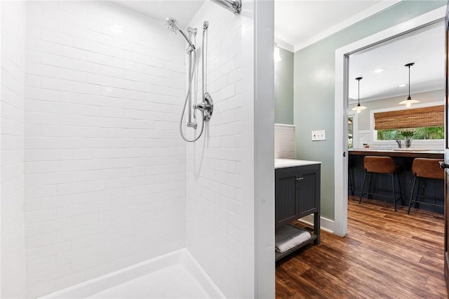 bathroom with wood finished floors, vanity, crown molding, and tiled shower