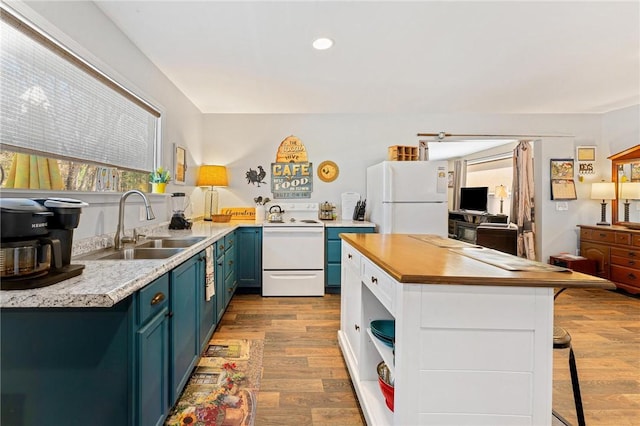 kitchen featuring a sink, a kitchen bar, wood finished floors, white appliances, and blue cabinetry