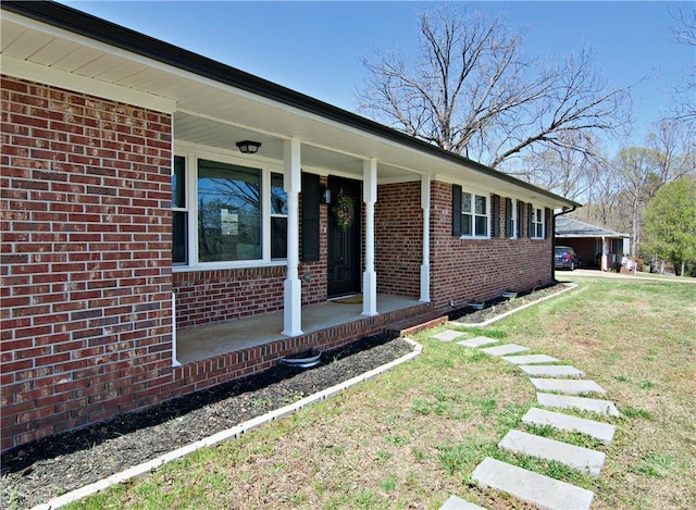 view of side of home with brick siding, covered porch, and a yard