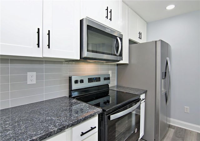kitchen with dark stone countertops, white cabinets, stainless steel appliances, and backsplash