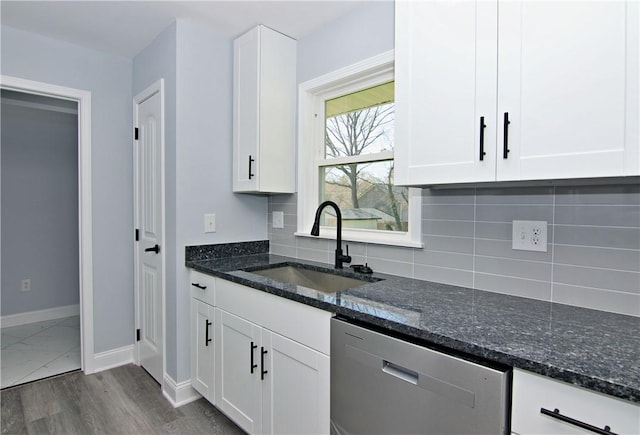 kitchen with white cabinets, baseboards, stainless steel dishwasher, a sink, and backsplash