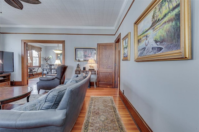 living area with baseboards, ceiling fan, crown molding, and light wood-type flooring