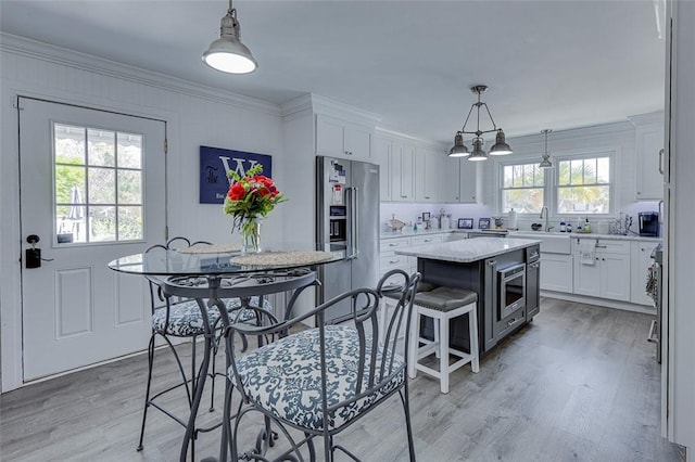 kitchen with crown molding, high end fridge, a kitchen island, light wood finished floors, and white cabinets