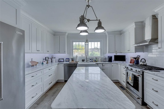 kitchen with wall chimney range hood, white cabinetry, a sink, and stainless steel appliances